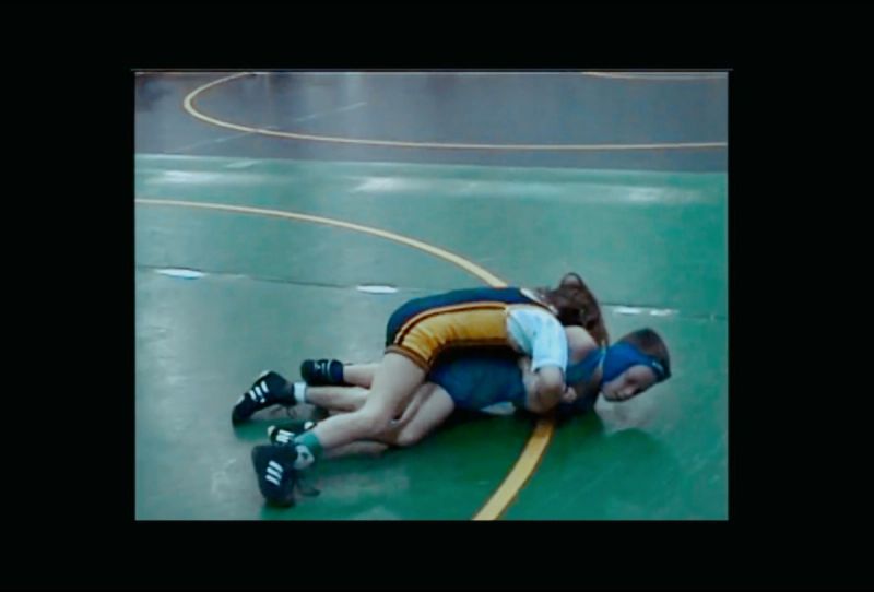 Olympic wrestler Helen Maroulis grappling with an opponent on a green wrestling mat.