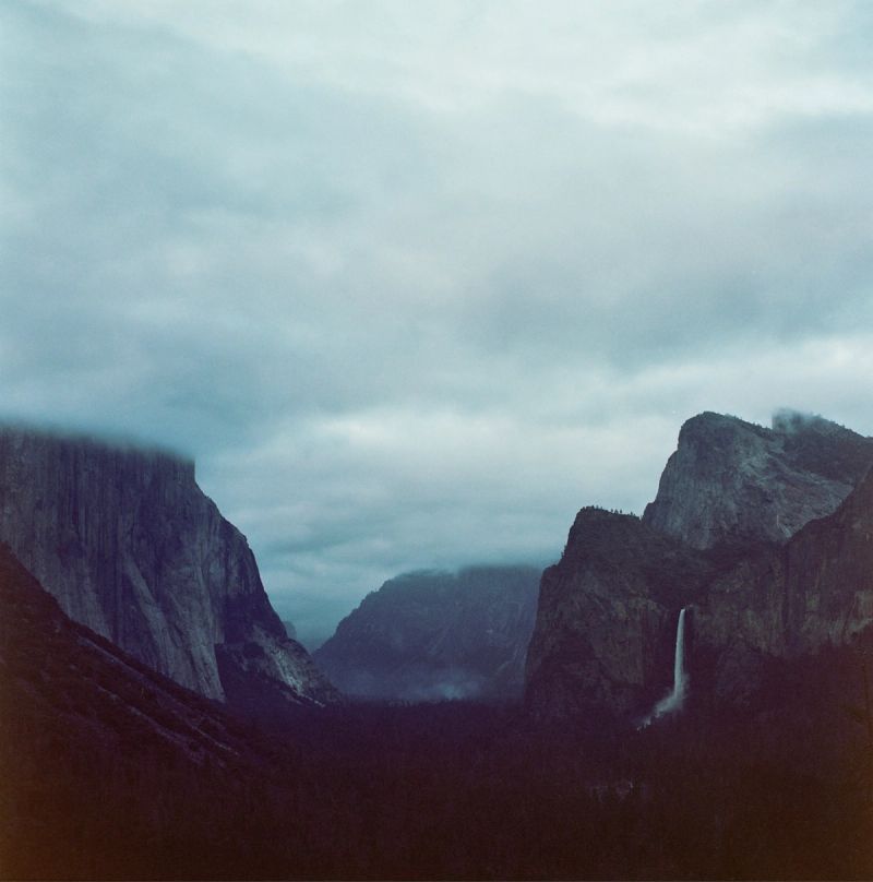 Misty Yosemite Valley landscape with granite cliffs and a waterfall under cloudy skies.