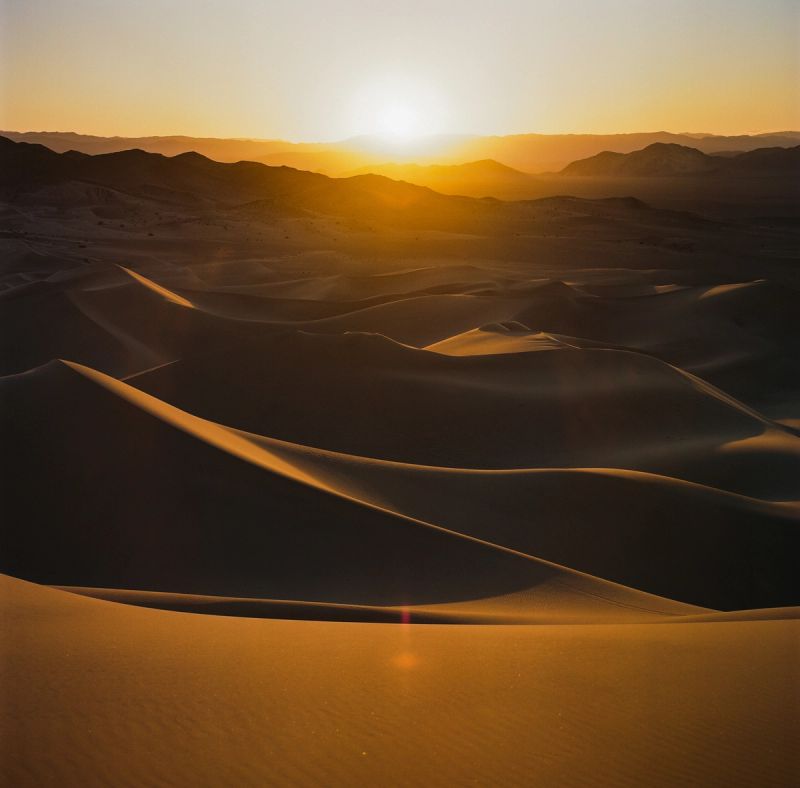 Golden hour light on rolling sand dunes with distant mountains