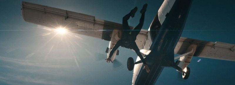 Cinematography of a skydiver in freefall near an aircraft wing against the sun.