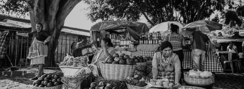 Black and white street market scene in Guatemala featuring vendors selling fruit and bread.