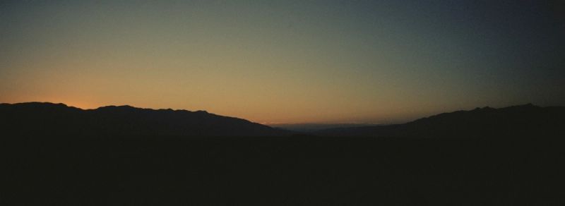 Silhouette of mountain range against a gradient twilight sky at dusk.