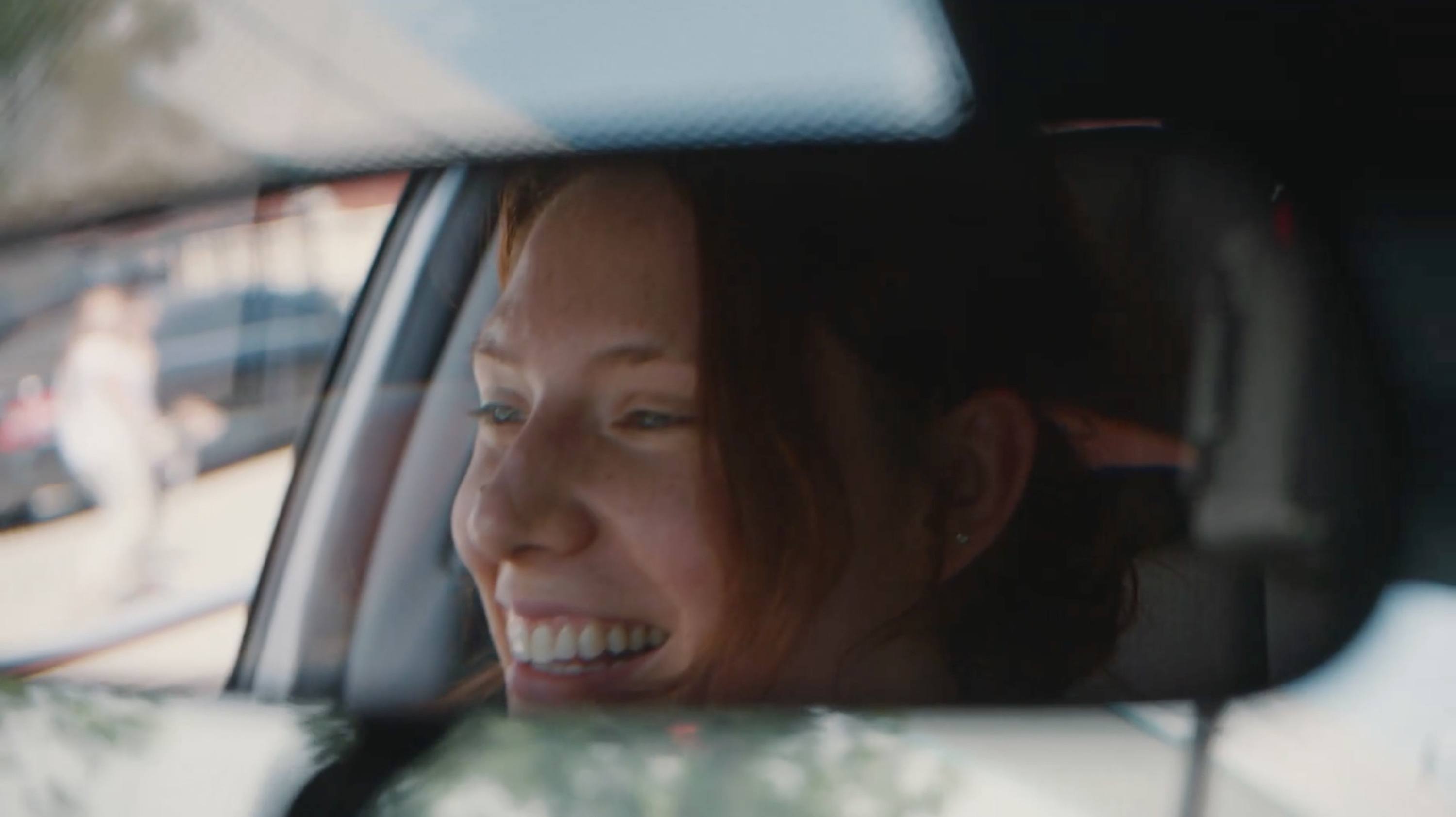 A candid portrait of a smiling woman inside a car looking out the window.