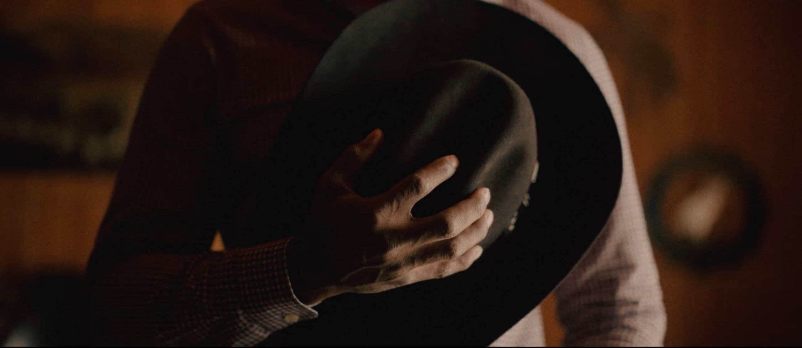 Hand holding a black cowboy hat in warm, dim lighting