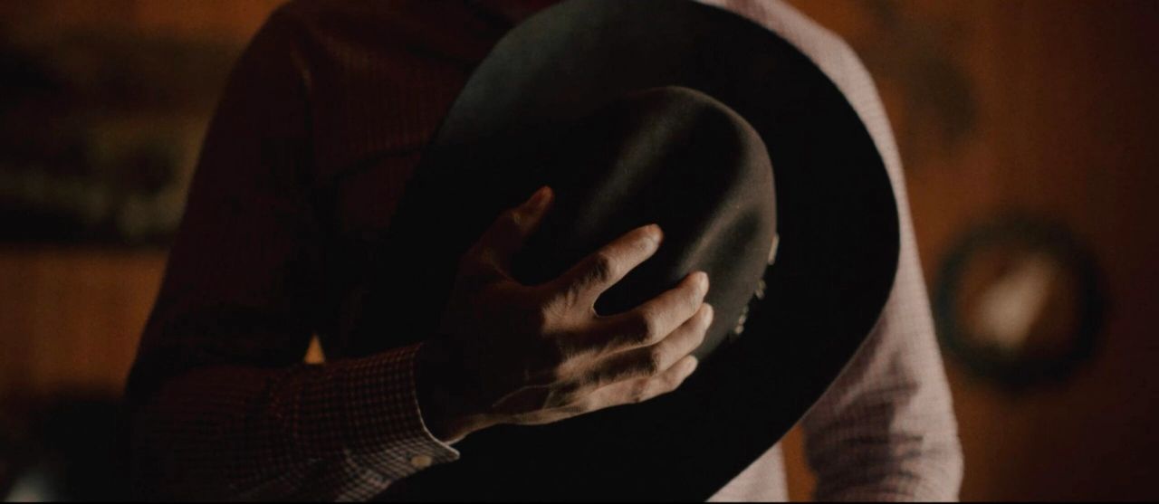 Hand holding a black cowboy hat in warm, dim lighting