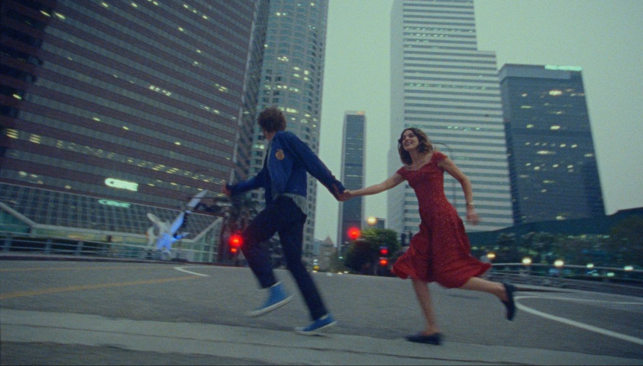 Couple running hand-in-hand across city street at dusk with skyscrapers in background