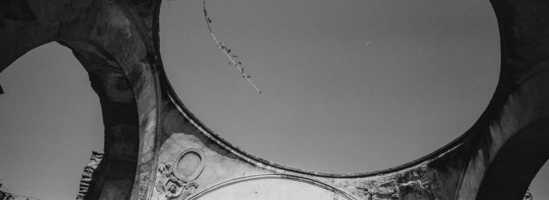 Low angle view through stone arches looking up at sky with hanging branch, Guatemala film photography.