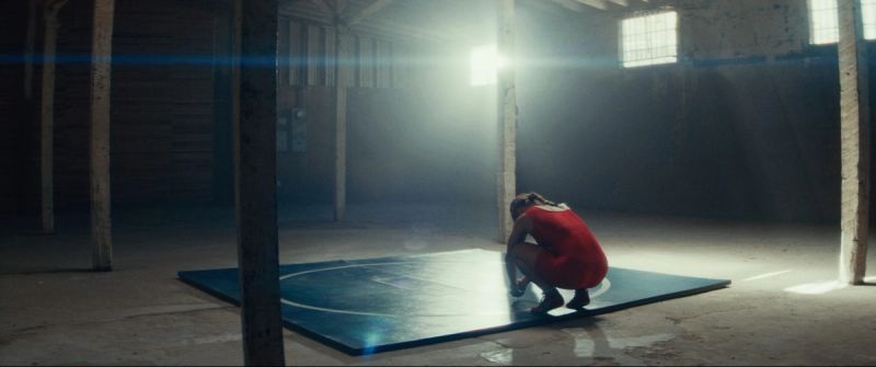 Olympic wrestler Helen Maroulis crouching on a blue mat in a sunlit, dusty warehouse space.