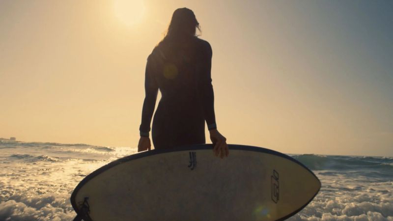 Surfer silhouette holding surfboard at sunset over ocean waves