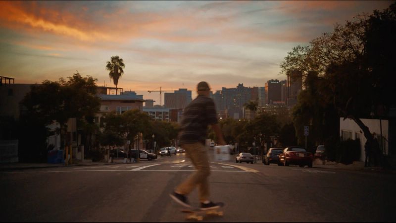 Skater rides down city street at sunset with skyline in background