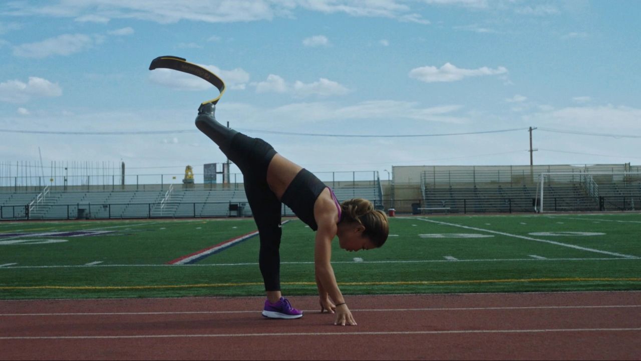 Athlete with prosthetic leg stretching on outdoor track under blue sky