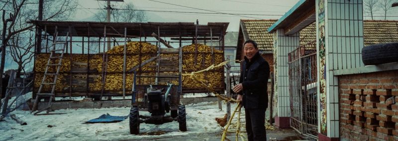 Man in rural China near corn storage and tractor, cinematic still from Toyota commercial
