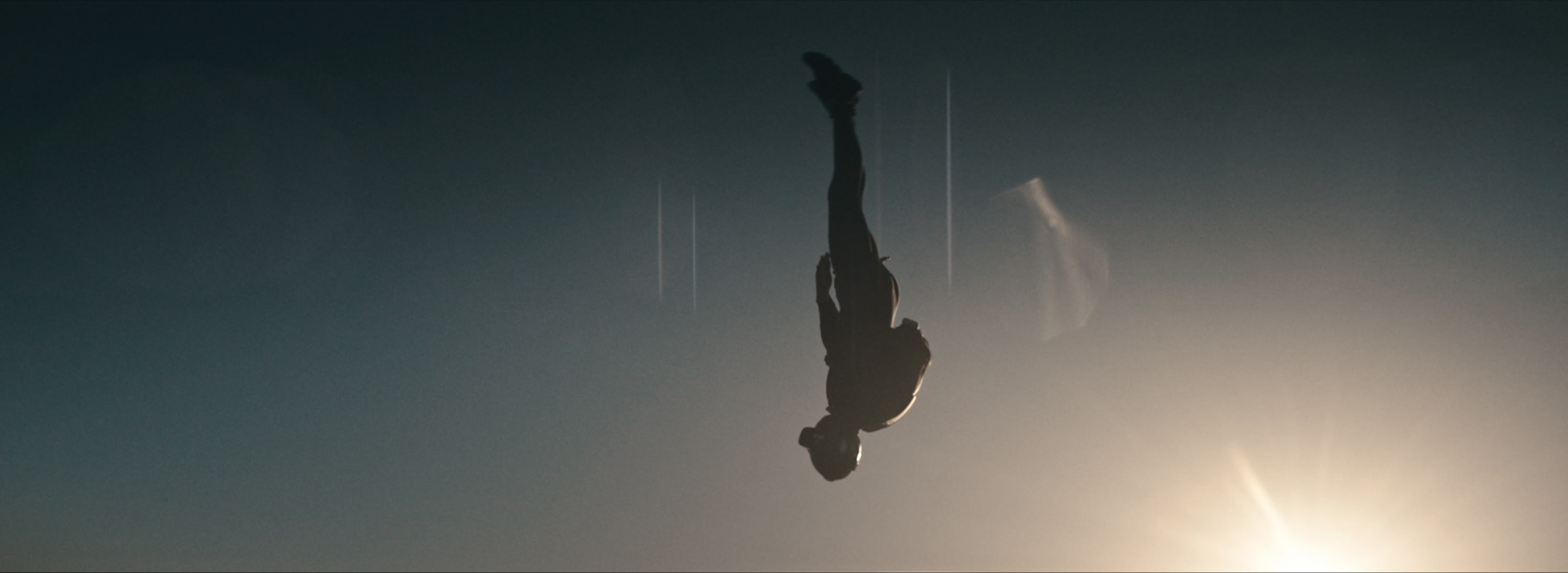Silhouette of a skydiver falling head down against a bright sun flare.