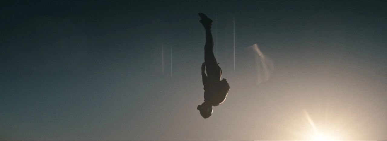 Silhouette of a skydiver falling head down against a bright sun flare.