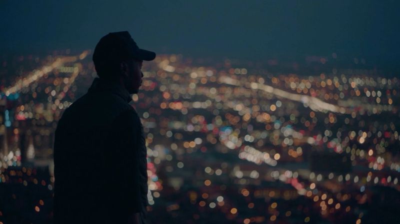 Silhouette of a man in cap overlooking blurred city lights at night