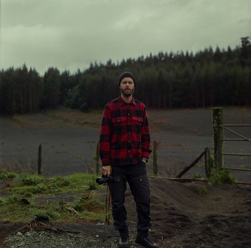 Cinematographer standing in Patagonia landscape holding camera wearing red plaid shirt.
