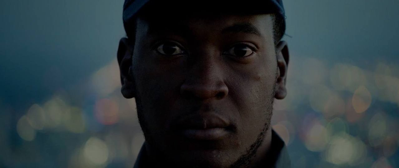 Close-up portrait of a man in a cap against blurred city lights at dusk