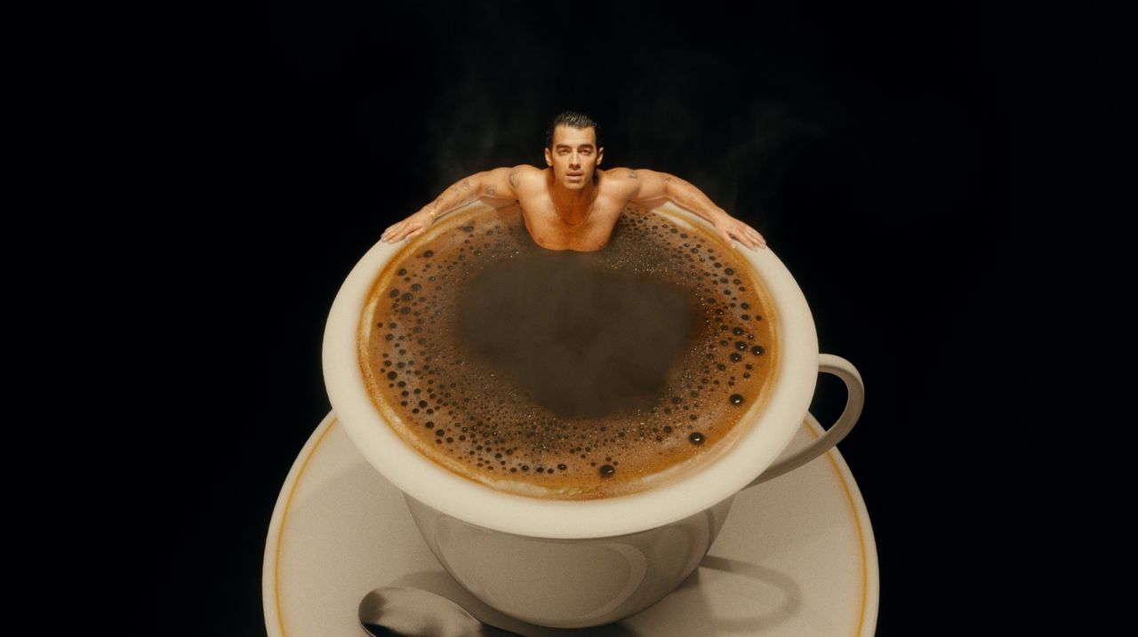 Joe Jonas emerging from a steaming cup of coffee against a black background.