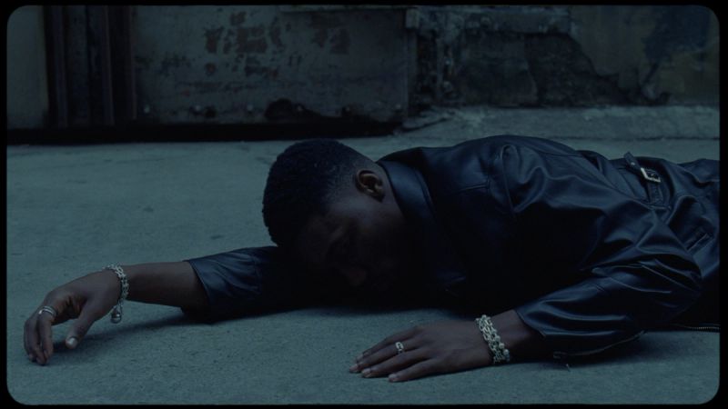 Man in black leather jacket lying on concrete ground, arms outstretched