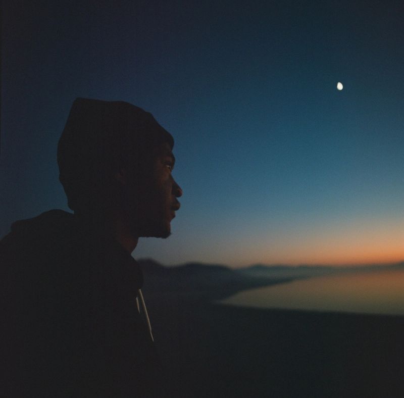 Silhouette of a man gazing at moon over desert landscape at twilight
