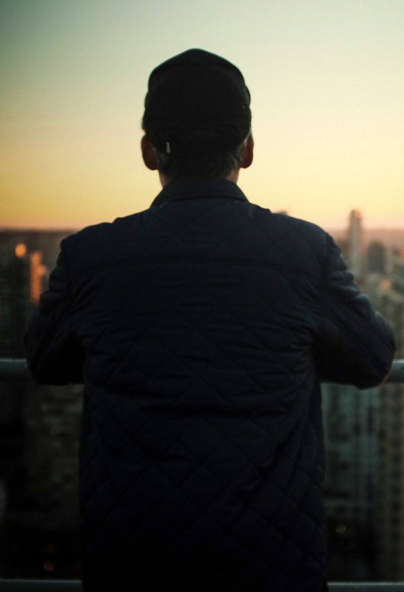 Cinematographer Ian Rigby viewed from behind on a rooftop overlooking city skyline at dusk