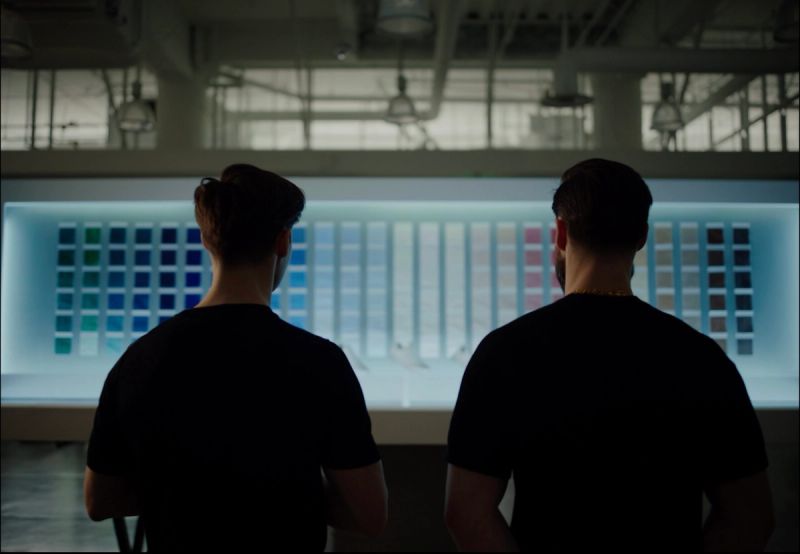 Two men viewed from behind examining a large illuminated color chart display in studio.