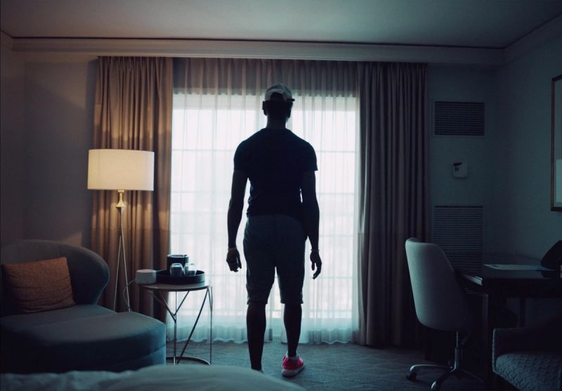 Reggie Jackson stands with his back to the camera looking out a window in a hotel room.
