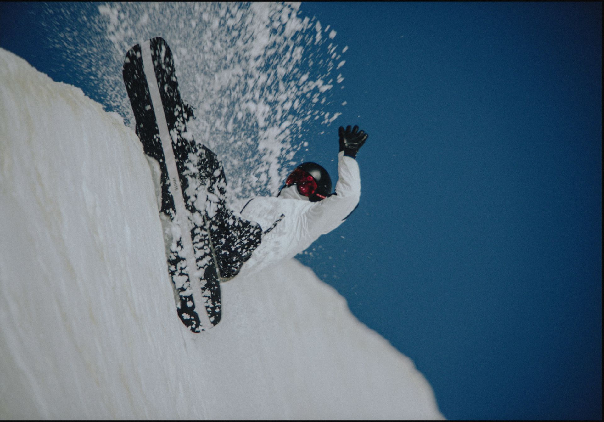 Snowboarder in white gear carving powder on a snowy slope against blue sky