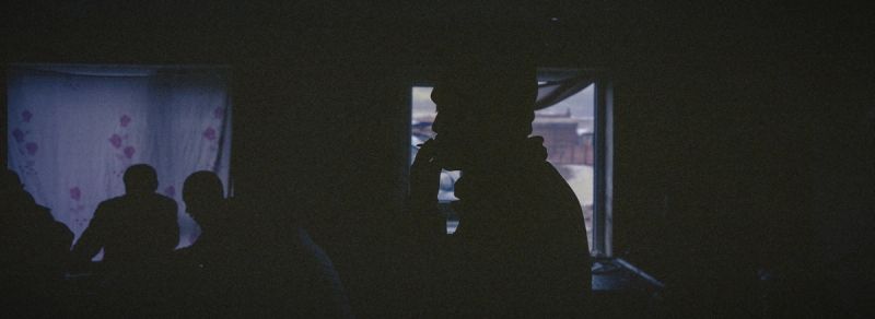 Silhouetted figures in dimly lit room with floral curtains and window view