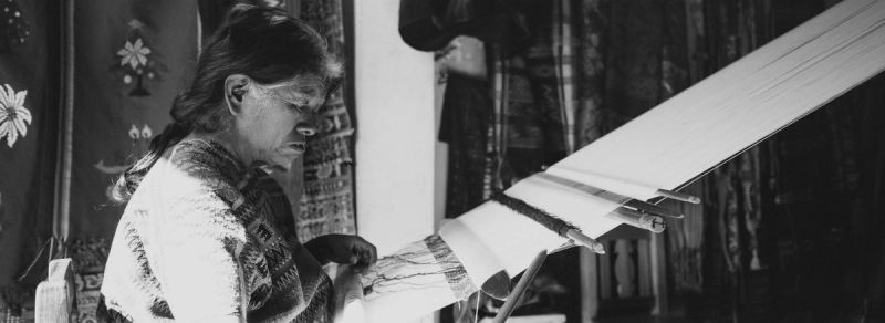 Elderly woman weaving traditional textiles on a loom in black and white film photography.