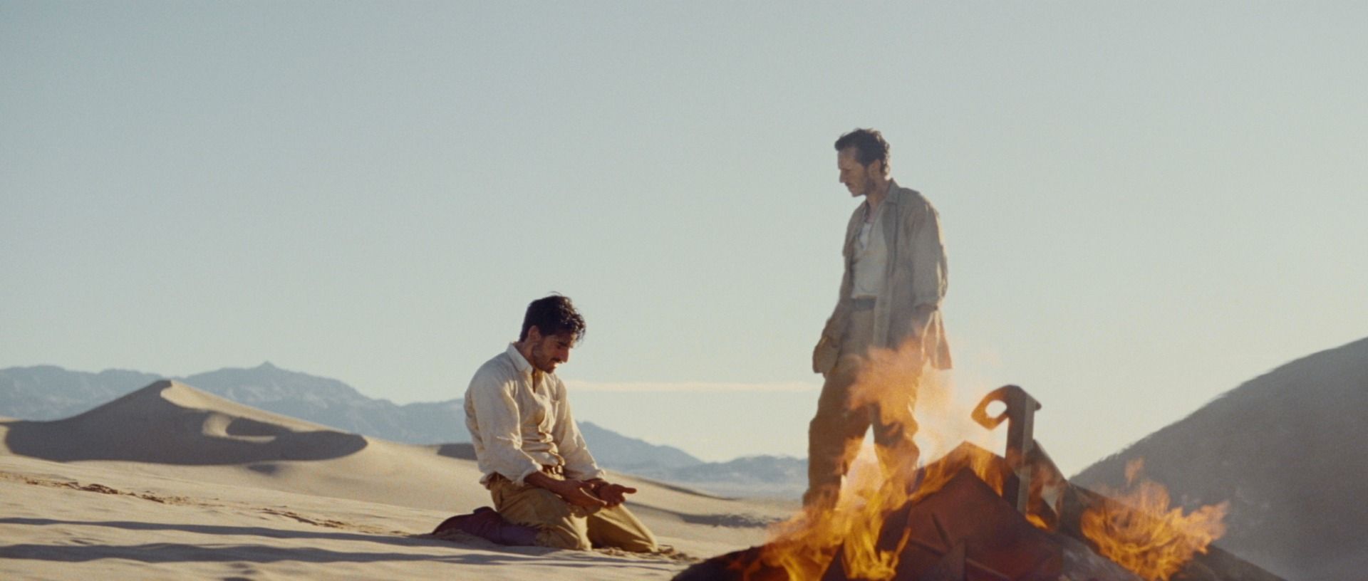 Two men in desert landscape with fire and vintage camera equipment