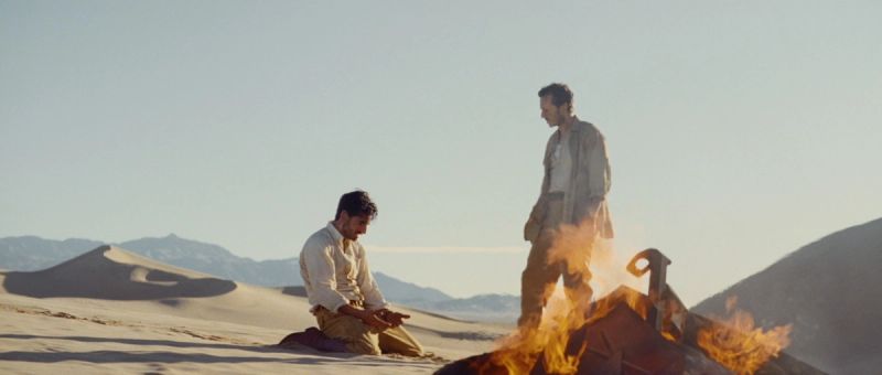 Two men in desert landscape with fire and vintage camera equipment
