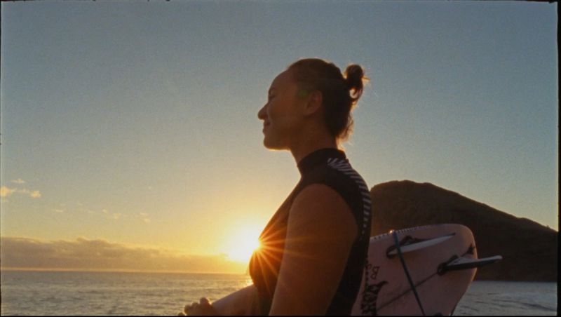 Surfer in silhouette at sunset with surfboard, golden hour light over ocean