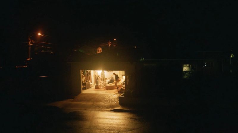 Night scene of a warmly lit garage interior with people gathered inside.