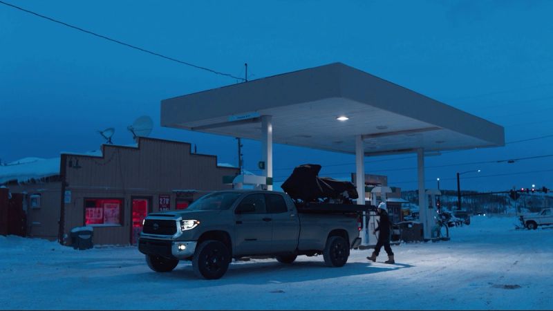 Silver Toyota Tundra truck parked at a snowy gas station under deep blue twilight sky.