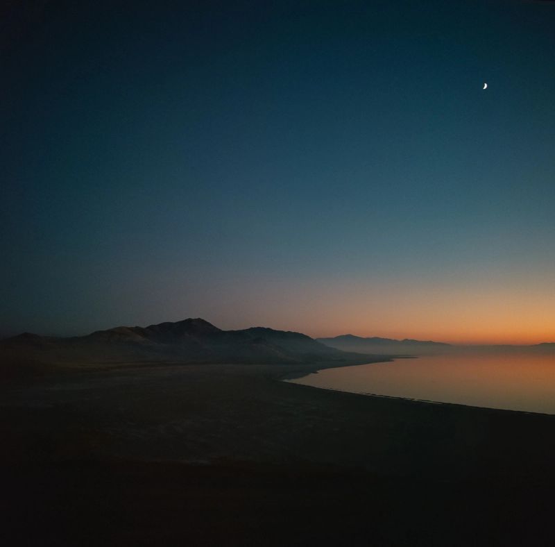 Cinematography of Antelope Island at dusk with crescent moon and mountain silhouette