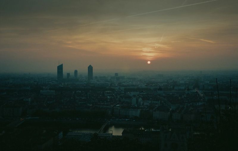 Cinematic dusk view of Paris cityscape with skyscrapers and hazy golden sky, film photography.