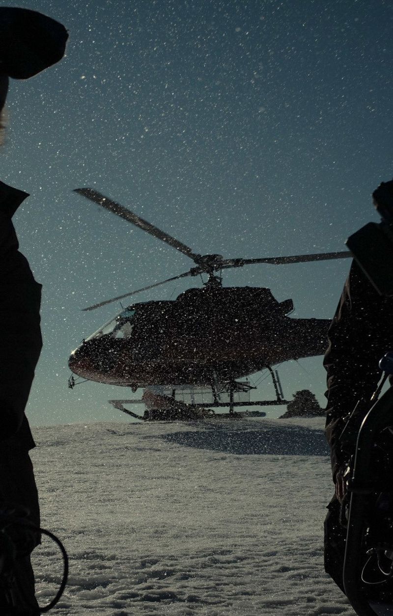 Helicopter silhouette in snow with falling flakes, framed by figures