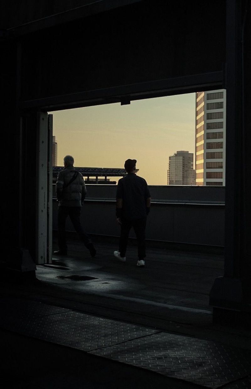 Two silhouetted figures walk toward city skyline at dusk through industrial doorway