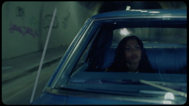 Woman with dark curly hair looking forward in a blue vintage car at night