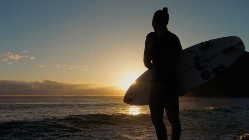 Surfer silhouette holding surfboard at sunset over ocean