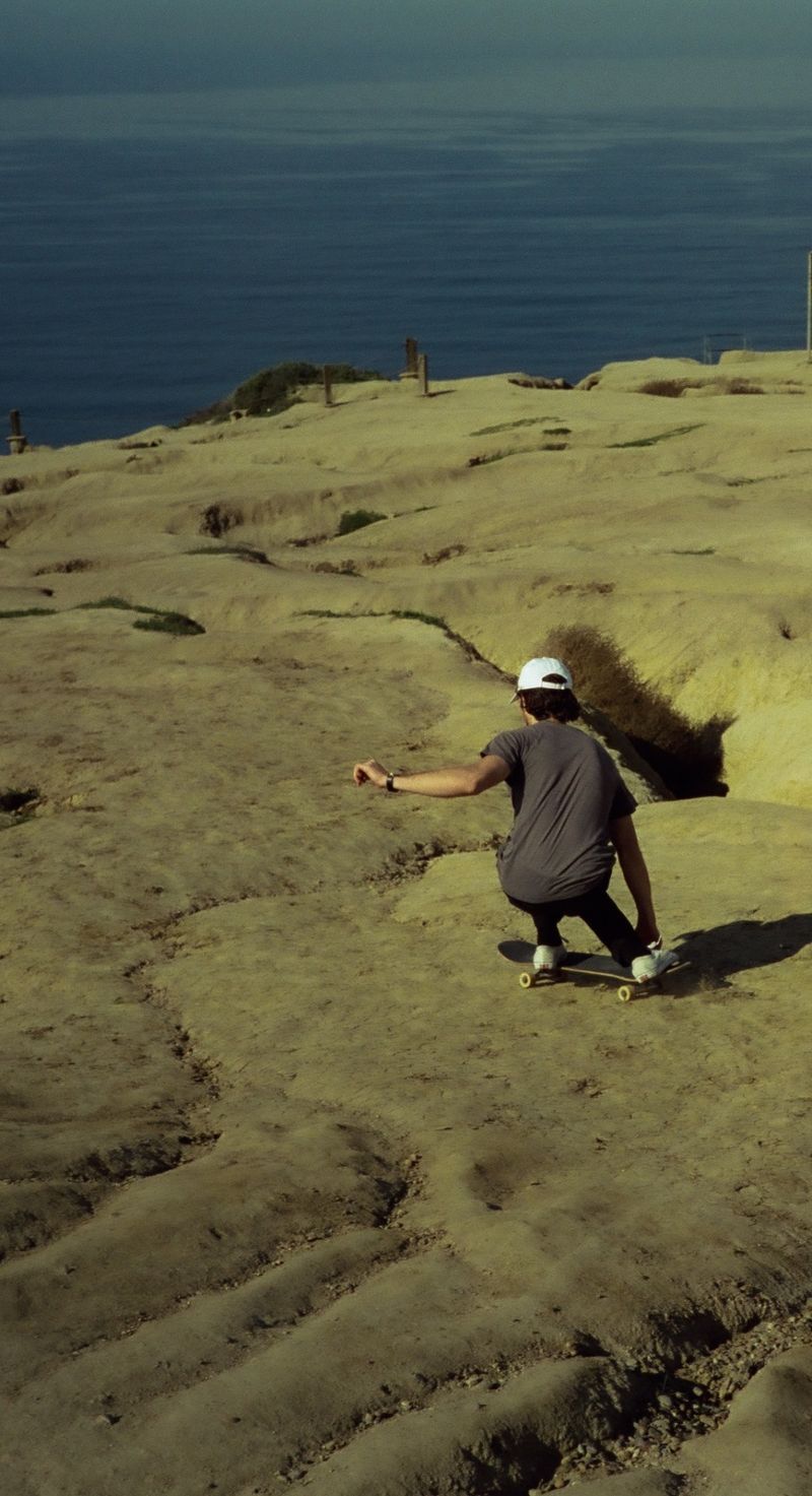 Skateboarder riding down a rocky coastal cliff overlooking the ocean