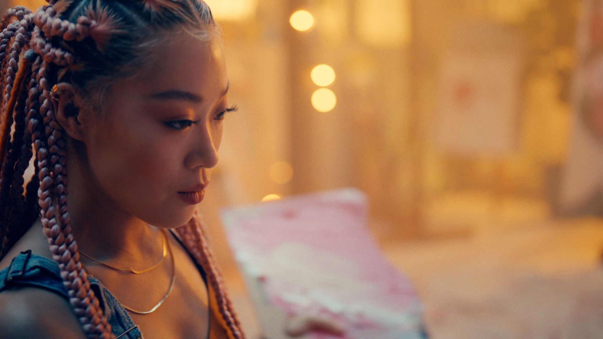 Nick Jonas reading lyrics in warm golden light, styled with braided hair