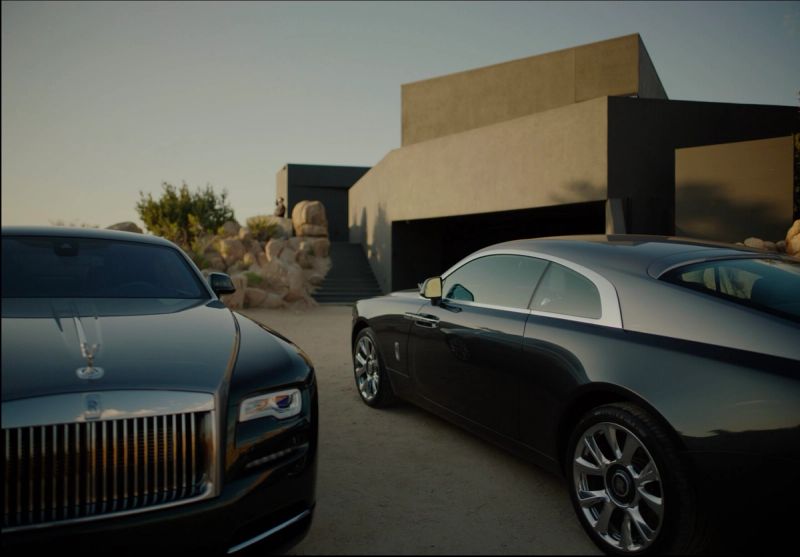 Two Rolls Royce vehicles parked in front of a modern architectural home in a desert landscape.