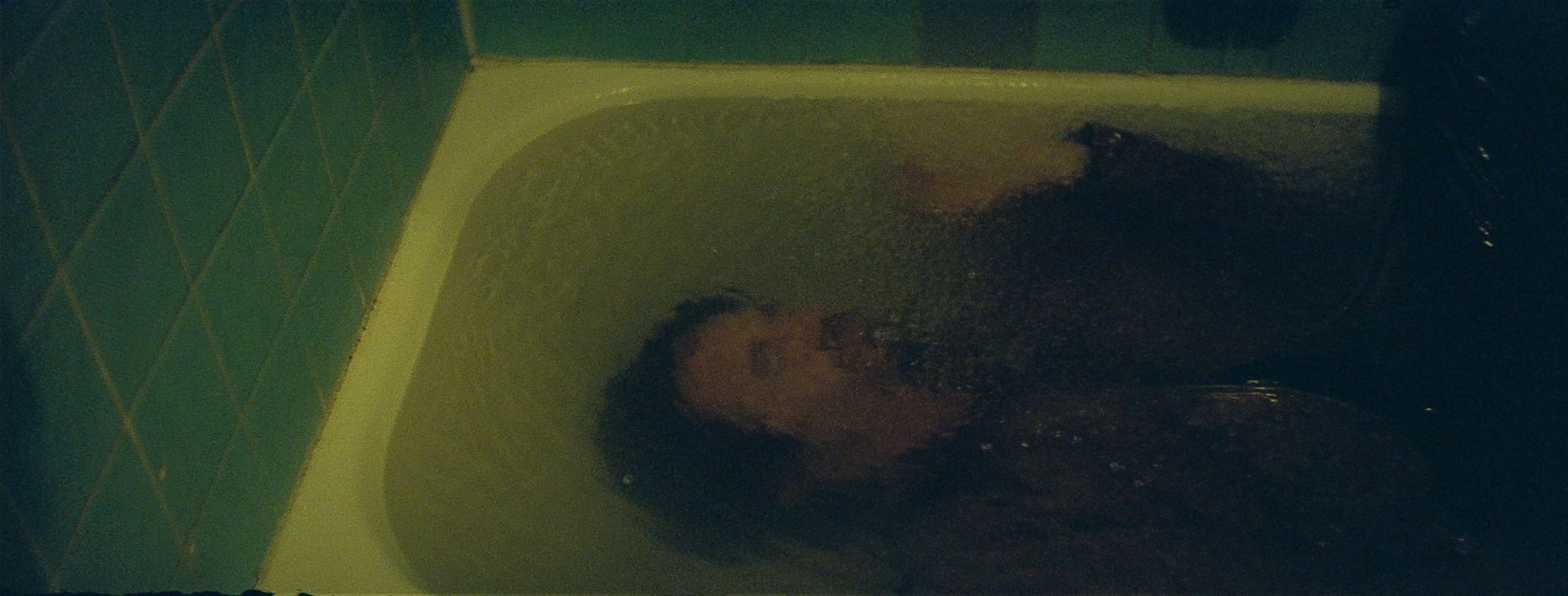 Man submerged in bathtub with teal tiles, cinematic film photography