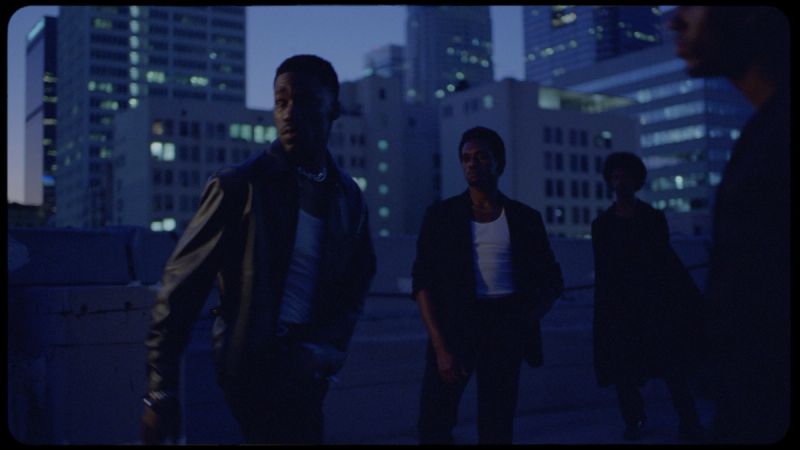 Four men stand on a rooftop at dusk in a city skyline, cinematic film photography.