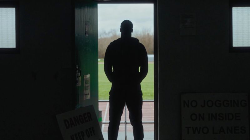 Silhouette of a man standing in doorway looking out at track and field