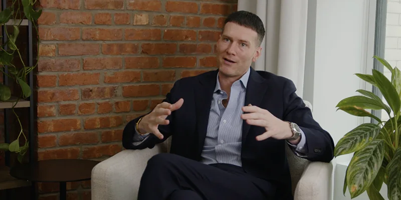 Talkiatry CEO Robert Krayn sitting in an armchair, speaking with hand gestures during an interview.