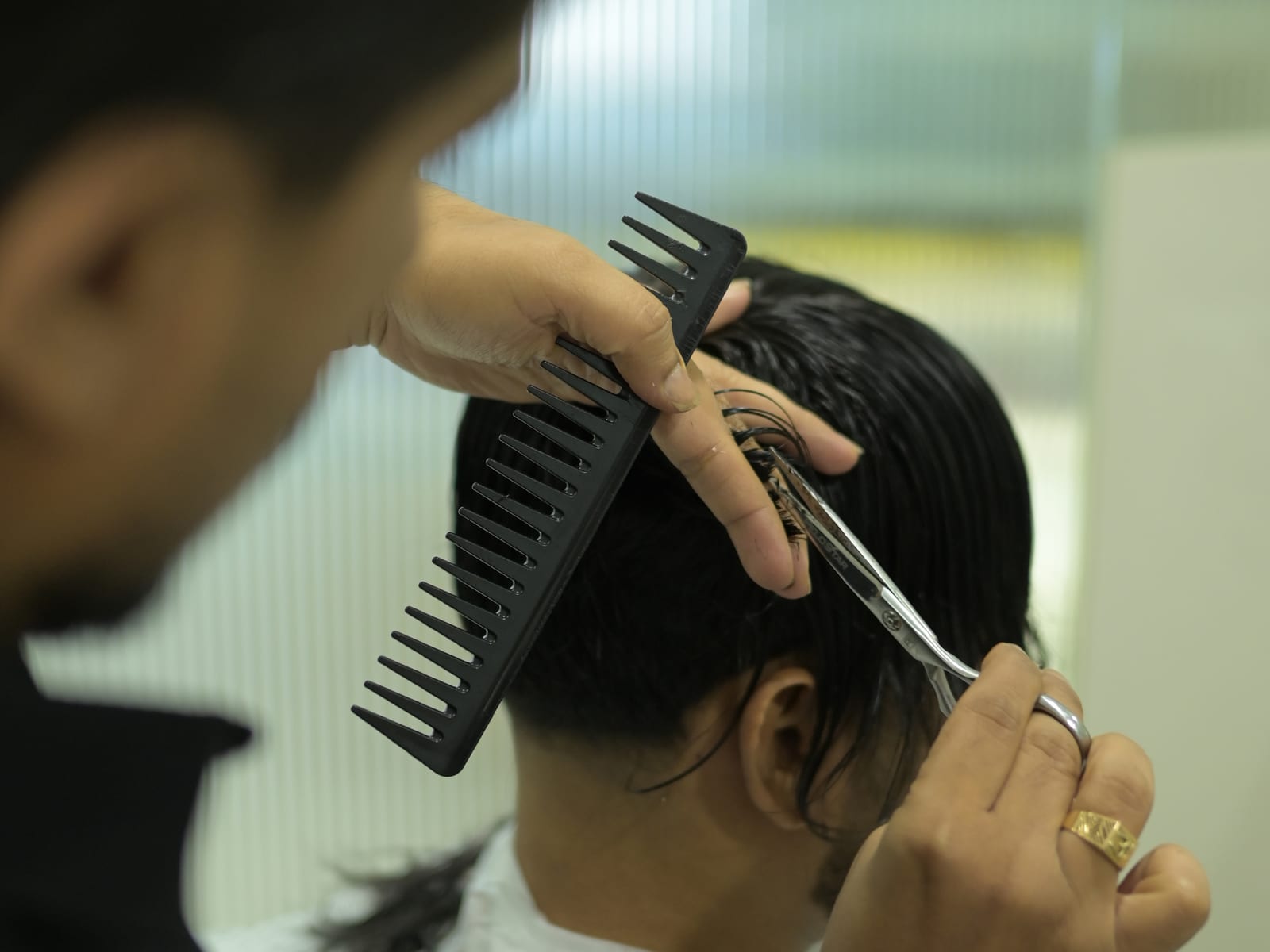 Wet hair being cut with scissors and a wide-tooth comb in the studio