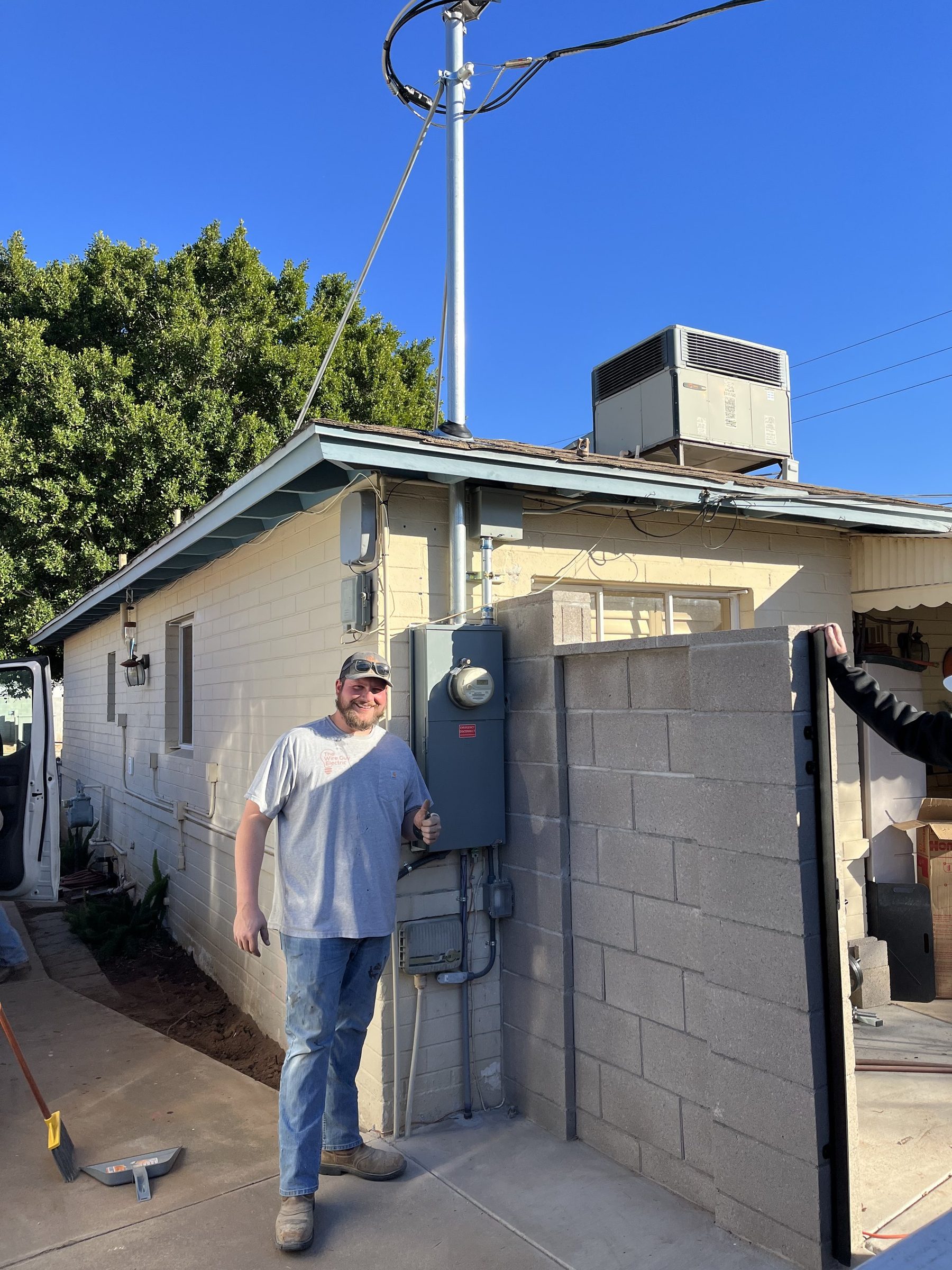 Electrician giving a thumbs up beside a new meter panel and service mast on a home